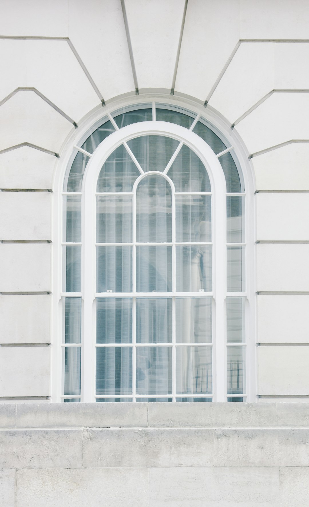 A white arched window with white panes on the side of an all-white building, in the style of high resolution photography. –ar 39:64