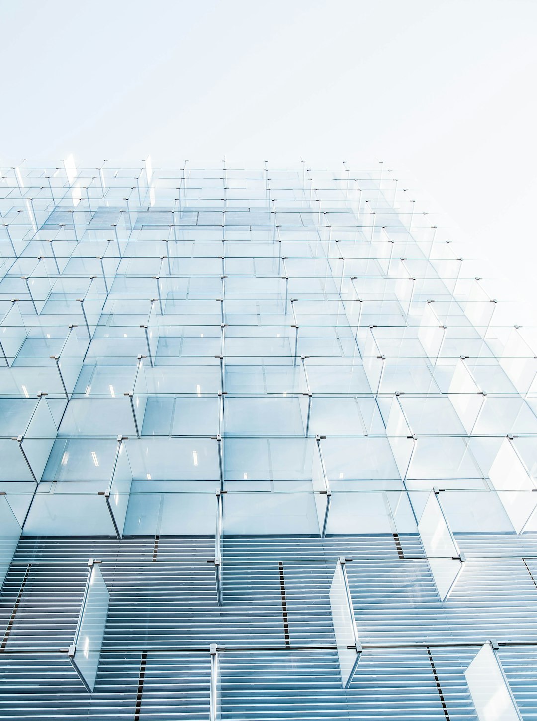 A glass building with many cubes on the facade, closeup shot from below, white sky background, minimalist style, modern architecture, high resolution photography, professional color grading, no contrast, clean sharp focus, bokeh effect, architectural photography, natural light, cinematic photography, soft shadows, no grainy film texture, captured in the style of Canon camera, hyperrealistic photography.