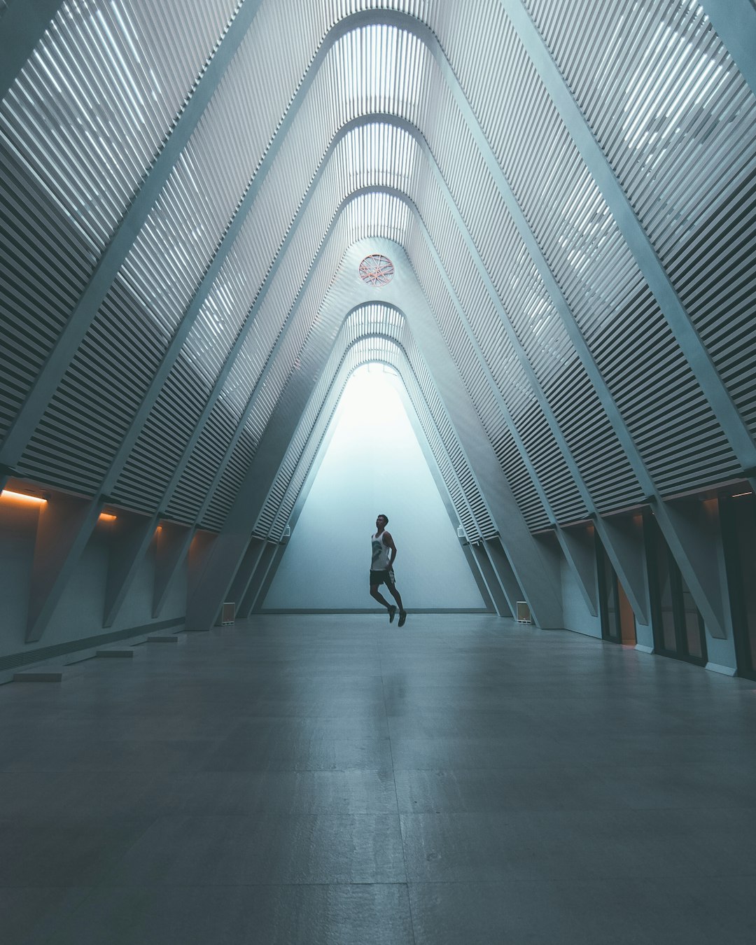 A person is running in the center of an architectural structure, a huge white futuristic building with triangular structures. A soft light illuminates it from above and fog fills part of its interior space. The photo was taken in the style of Sony Alpha A7 III camera with a wideangle lens. It has a cinematic quality and high resolution.