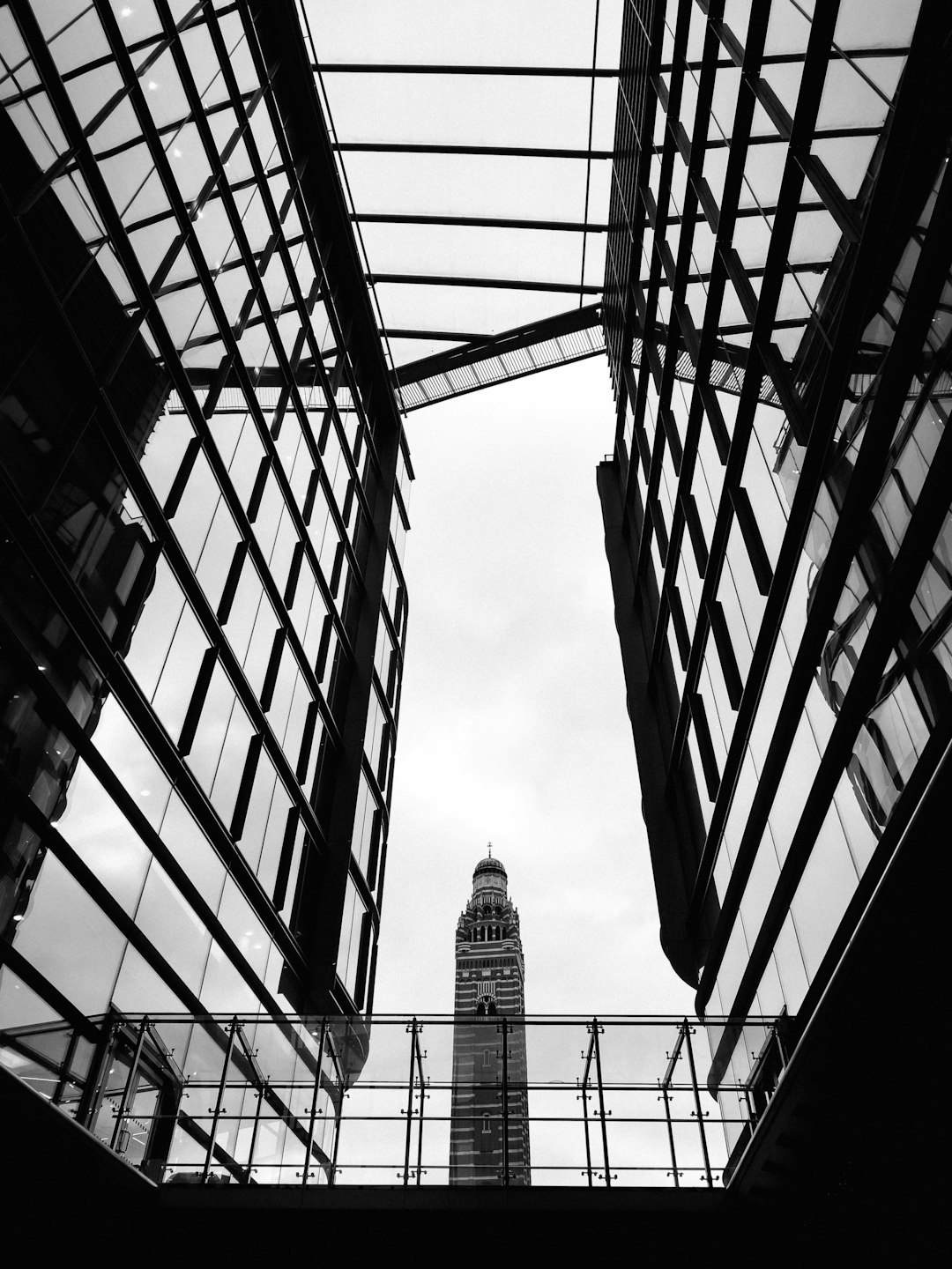 The Chiento Tower in Hong Kong, seen from below through the glass roof of an outdoor plaza, surrounded by modern buildings in the style of black and white photography. The tower stands tall against the sky, its silhouette casting long shadows on surrounding structures. Captured using a Fujifilm XT4 camera with a Leica M3 lens at a f/2.8 aperture setting. High resolution and detailed rendering. Black background, highlighting architectural details. Wideangle perspective view. –ar 3:4