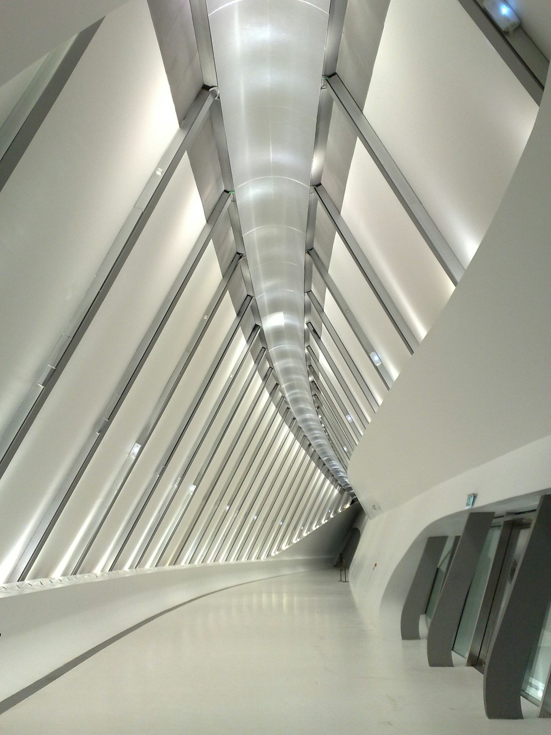 An interior view of the roof structure in white steel, rectangular shape with long lines on it, in an urban area, in the style of [Zaha Hadid](https://goo.gl/search?artist%20Zaha%20Hadid), futuristic, clean floor, bright lights inside, white walls and metal beams. –ar 3:4