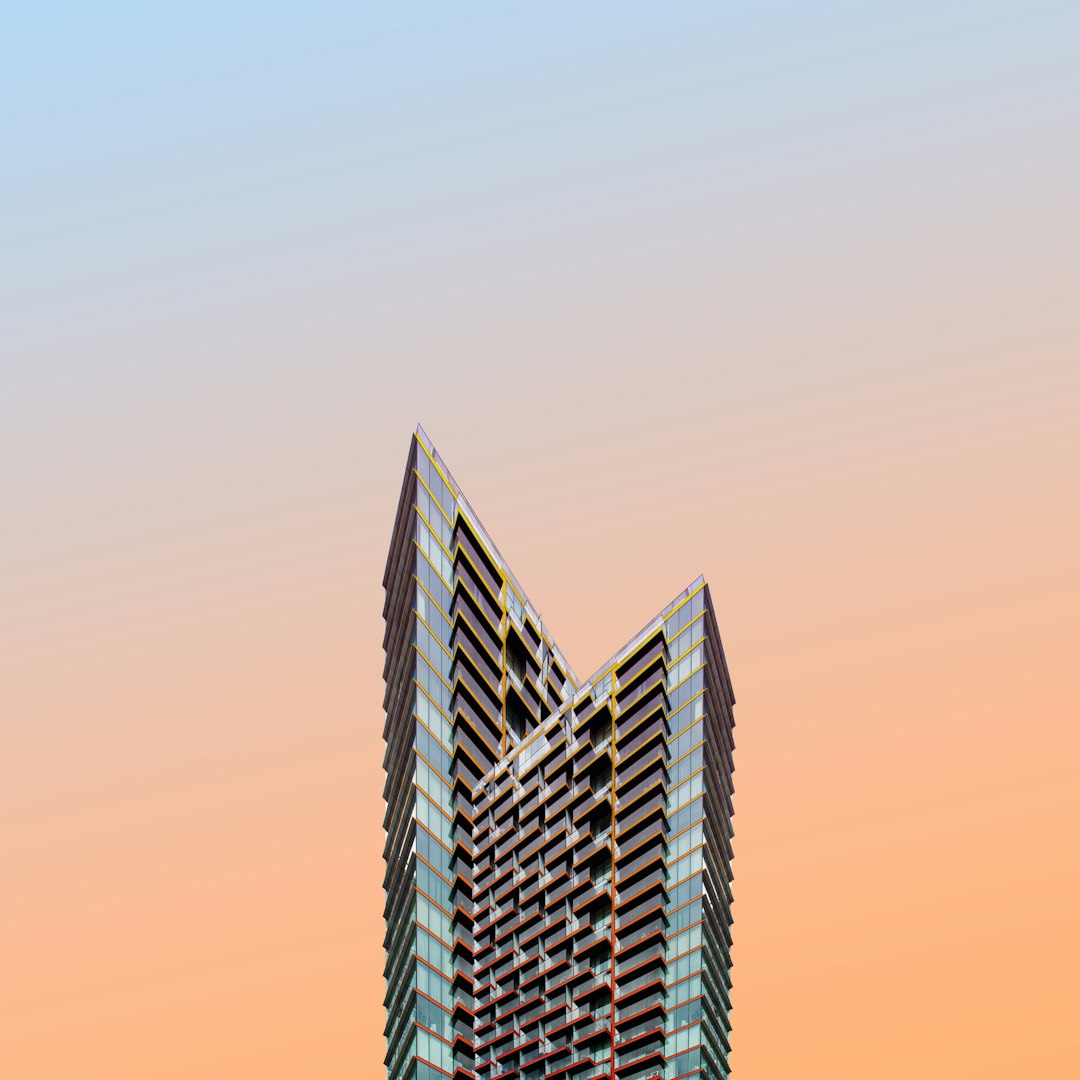 A tall building in the shape of an M, in the minimalist style, with a clear sky and sunset colors, a high resolution photograph, professional color grading, soft shadows, low contrast, clean sharp focus, in the style of a magazine photoshoot.