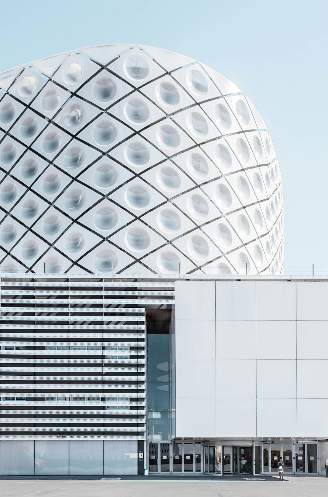 front view of a white building with a large glass dome. The facade is made from horizontal metal stripes and dots, designed in the style of [Bjarke Ingels](https://goo.gl/search?artist%20Bjarke%20Ingels) in the middle part of the Cån collaboratory architecture studio. Minimalistic and award winning architectural photography from a magazine. –ar 21:32