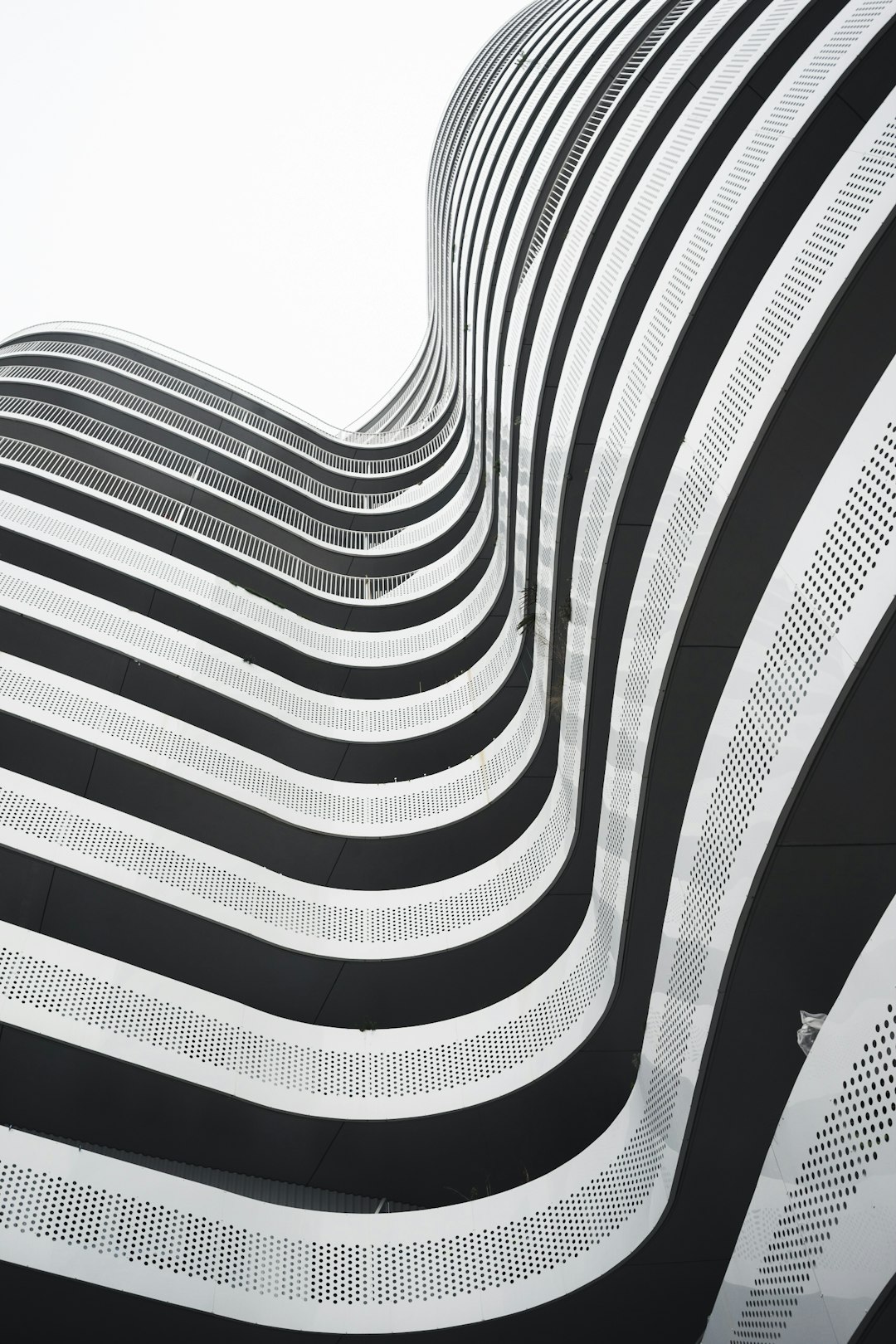 Black and white lines, curved building facade with high resolution photography and hyperrealistic details of architectural photography on a white background. The building has a vertical striped metal wall with fine texture in the modern architecture style of geometric shapes in a symmetrical composition. –ar 85:128