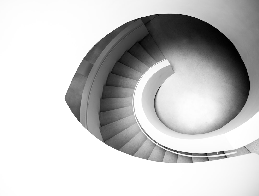 Black and white photography of spiral staircase, highangle shot, minimalism, high contrast, symmetrical composition, architectural style, modern architecture, minimal design, modernist building, architectural details, smooth lines, geometric shapes, white background, soft light, high resolution, detail focus, high quality, high definition, professional photo, natural lighting. –ar 128:97