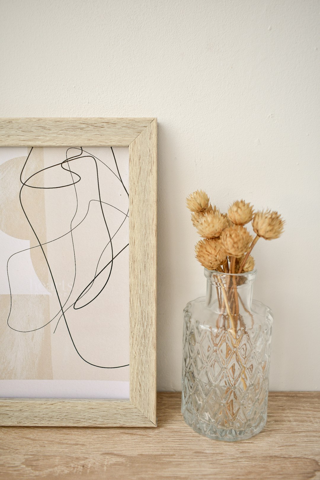 a light wooden picture frame with one vertical line drawing of the female form, resting on an oak shelf next to dried flowers in vintage glass vase, neutral colours, modern art print, –ar 85:128