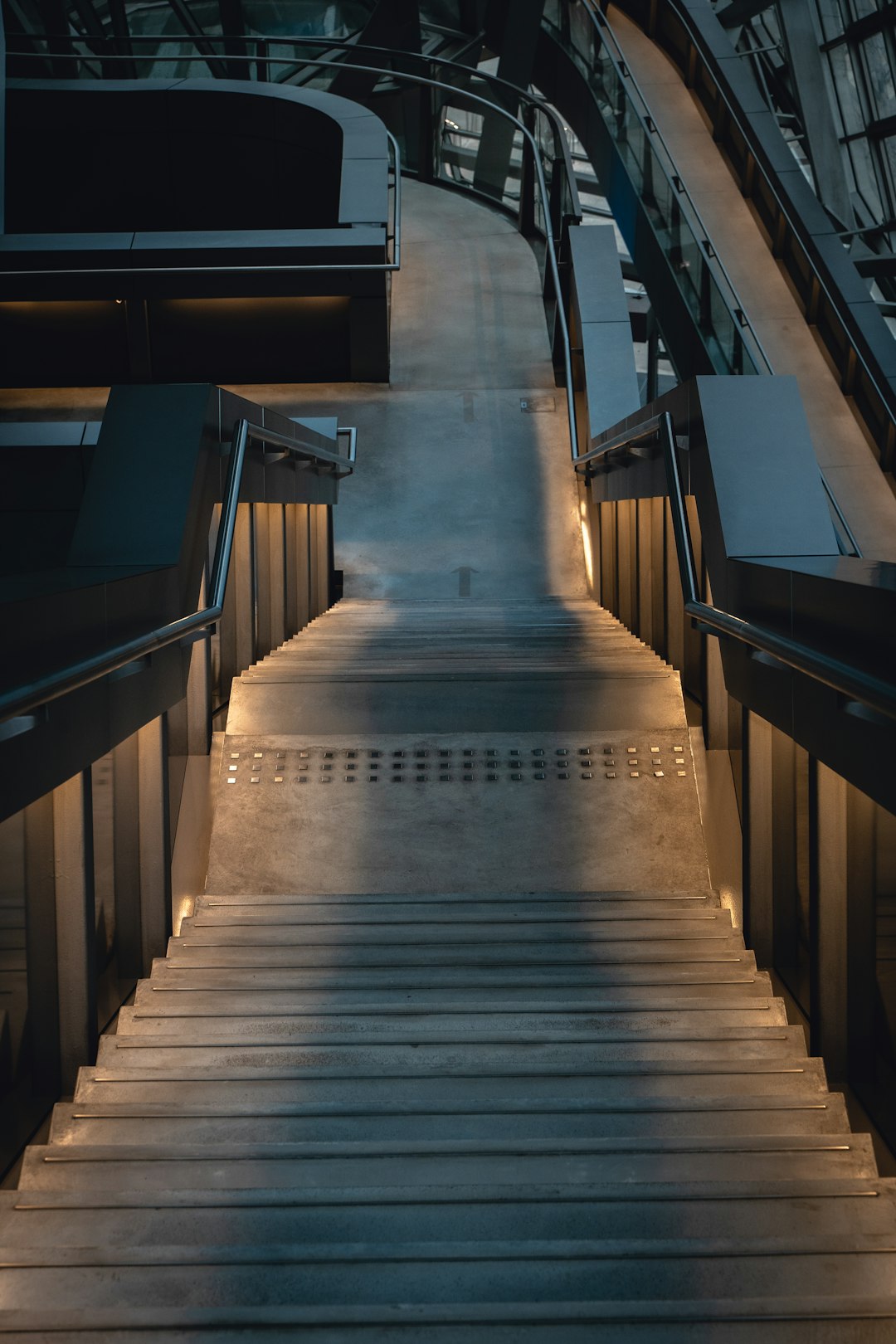 photo of a modern stairway made of dark grey metal and glass with soft lighting. In the background is an office space, in the style of unsplash photography, with a low angle camera shot. –ar 85:128