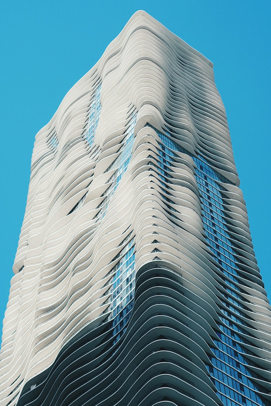 A tall building made of white wavy metal, parametric architecture style, on blue background, hyperrealistic photography, eyelevel shot, 24mm lens –ar 85:128