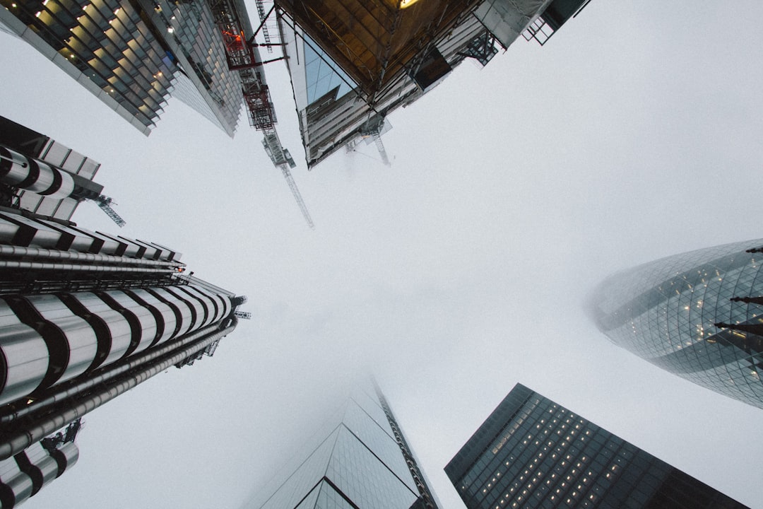 Photo of the city of London, looking up at skyscrapers from a low angle shot with muted tones and a foggy sky against a white background, captured with a Canon EOS R5 in the style of no particular artist. –ar 128:85