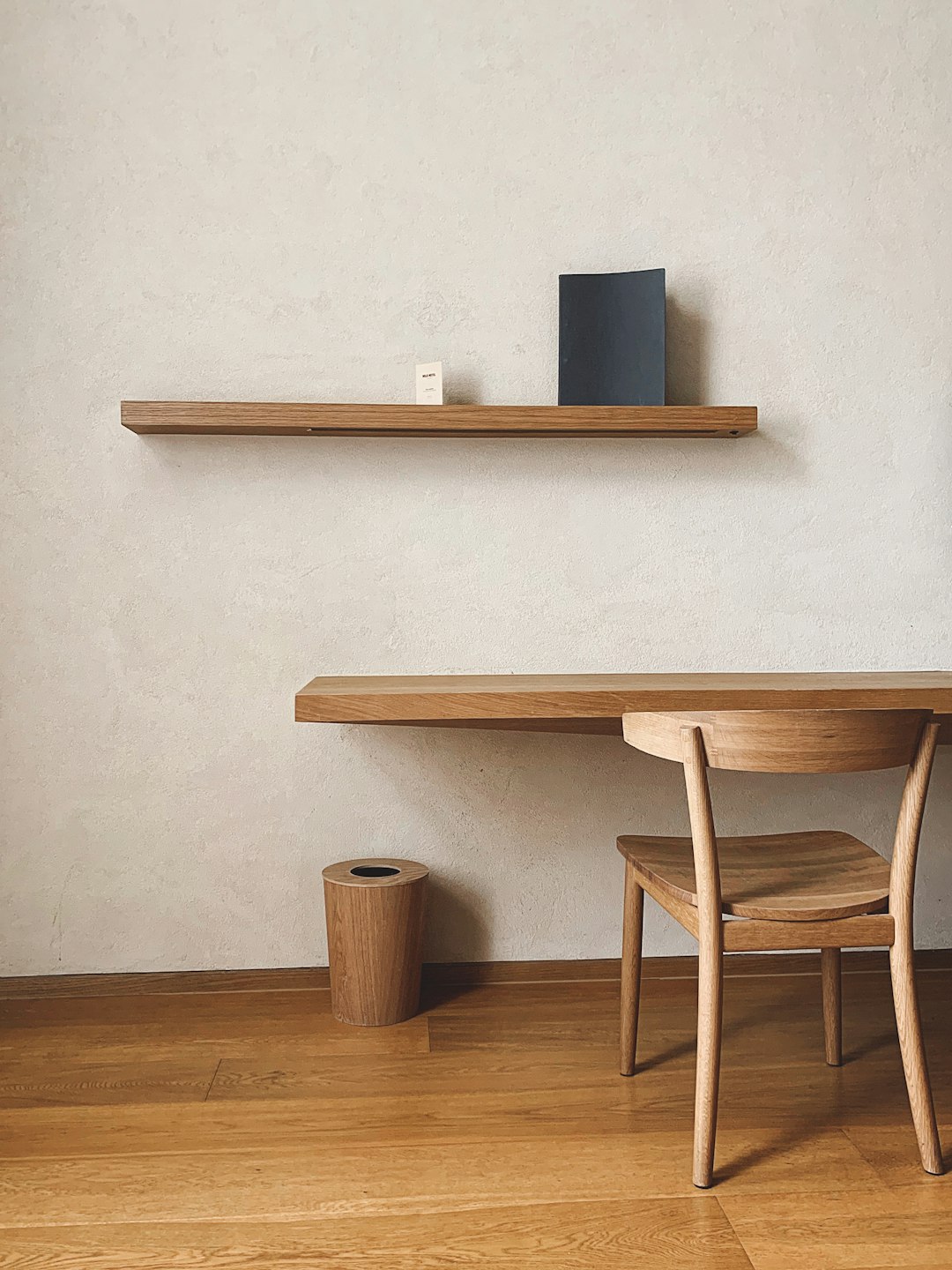 minimalist wooden shelf floating on the wall above an oak desk, modern interior design photography, beige walls, simple chair