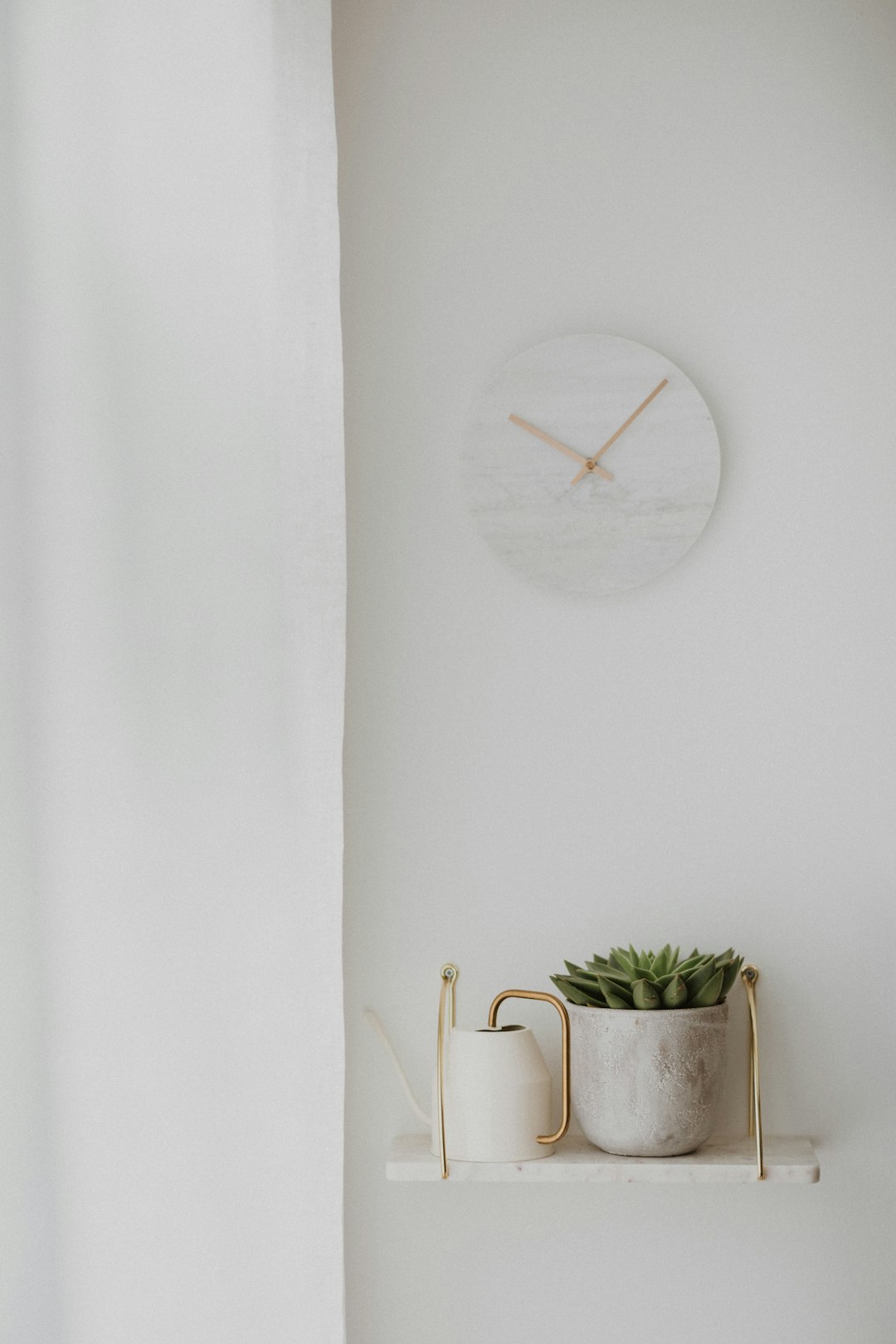 The white wall had a marble clock, brass shelf and succulent plant, with a minimalistic decor, soft lighting and clean lines in neutral tones, focusing on the simplicity of the design. It was a minimalist interior photography shot with a Canon EOS R5 camera and macro lens. –ar 85:128