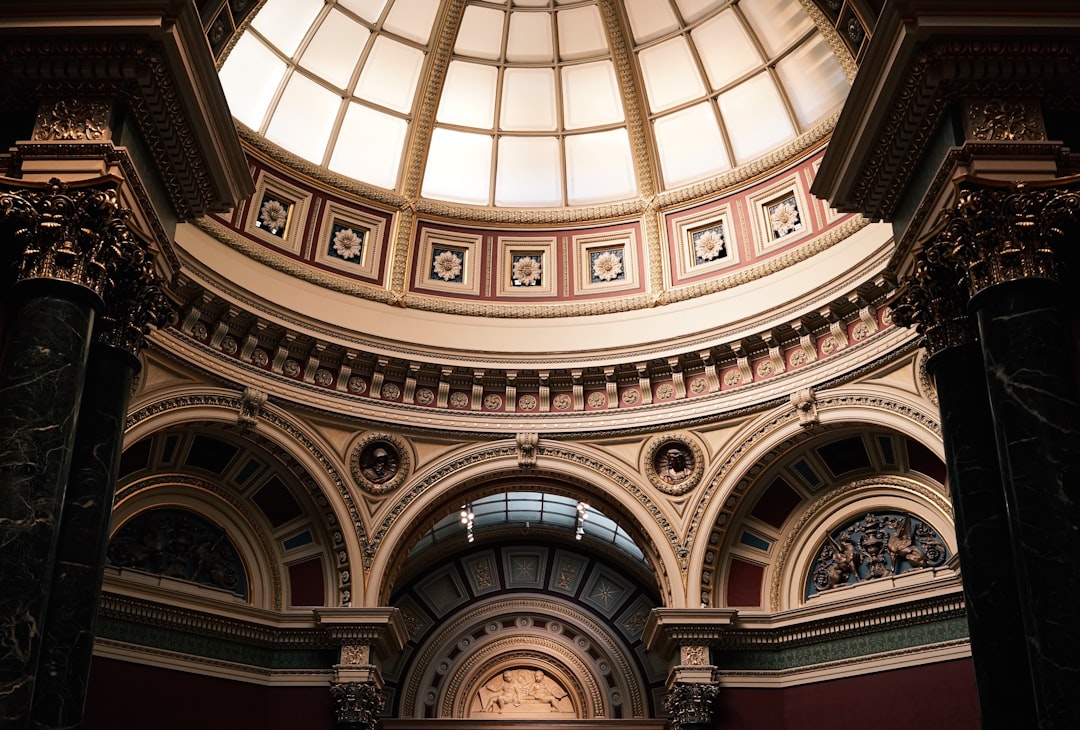 A photo of the dome in modern style inside an art museum, with classical architecture and columns surrounding it. The ceiling is painted white, creating a bright atmosphere. There’s an arched entrance leading to another room. On one side of each column lies an ancient Roman sculpture. Shot on Canon EOS R5 camera with Canon RF 2470mm f/2 lens at F8 aperture setting; ISO 640; natural light from a skylight above. –ar 64:43