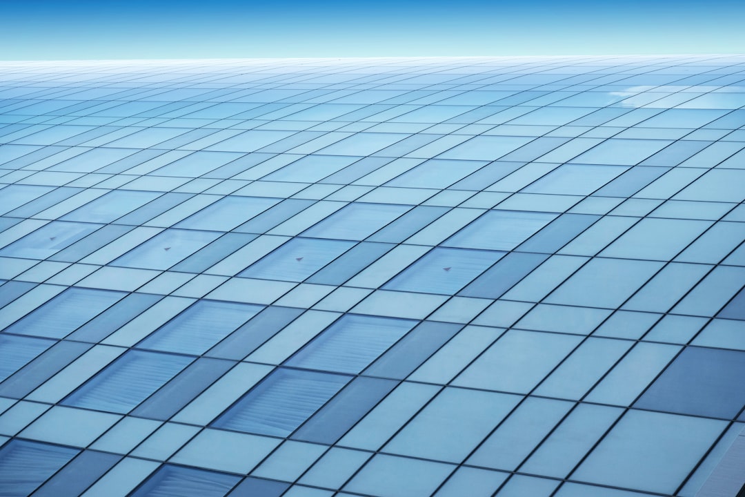 A large flat surface of glass with the same size and shape, the entire picture is covered by transparent blue sky. The top view shows a wideangle perspective of the vast rectangular grid of building windows. It’s a clean background with no visible elements such as buildings or people. This scene gives an impression that it could be part of a hightech futuristic setting. In detail, each window glares light onto its surroundings in a symmetrical pattern, creating an illusion of infinite depth. –ar 128:85