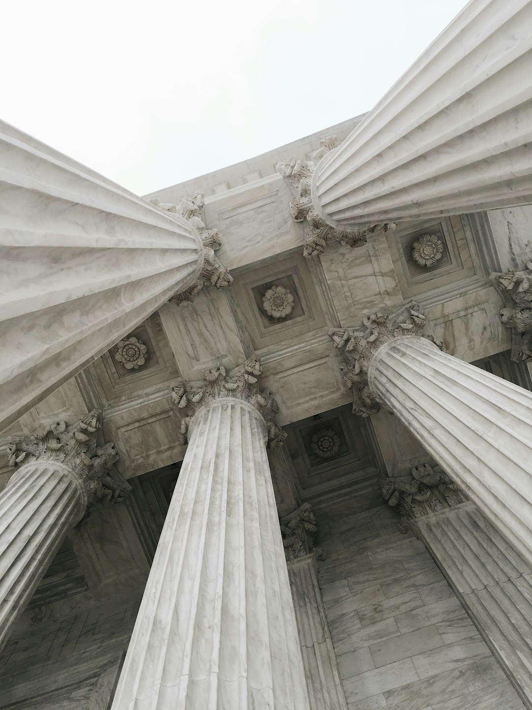 A photo of the architecture detail of The US Supreiosum within white marble, shot from below, view looking up at a sky with a slight overcast, light grey background, natural lighting, muted colors, architectural photography, raw –ar 3:4