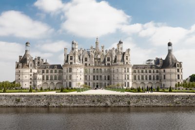 Chateau de Chambord in France, front view, with the river on one side and people walking along it, sunny day, blue sky with white clouds, high resolution photography, detailed, fine details, isolated plain background, stock photo, photography in the style of a professional with color grading, hyper realistic photography