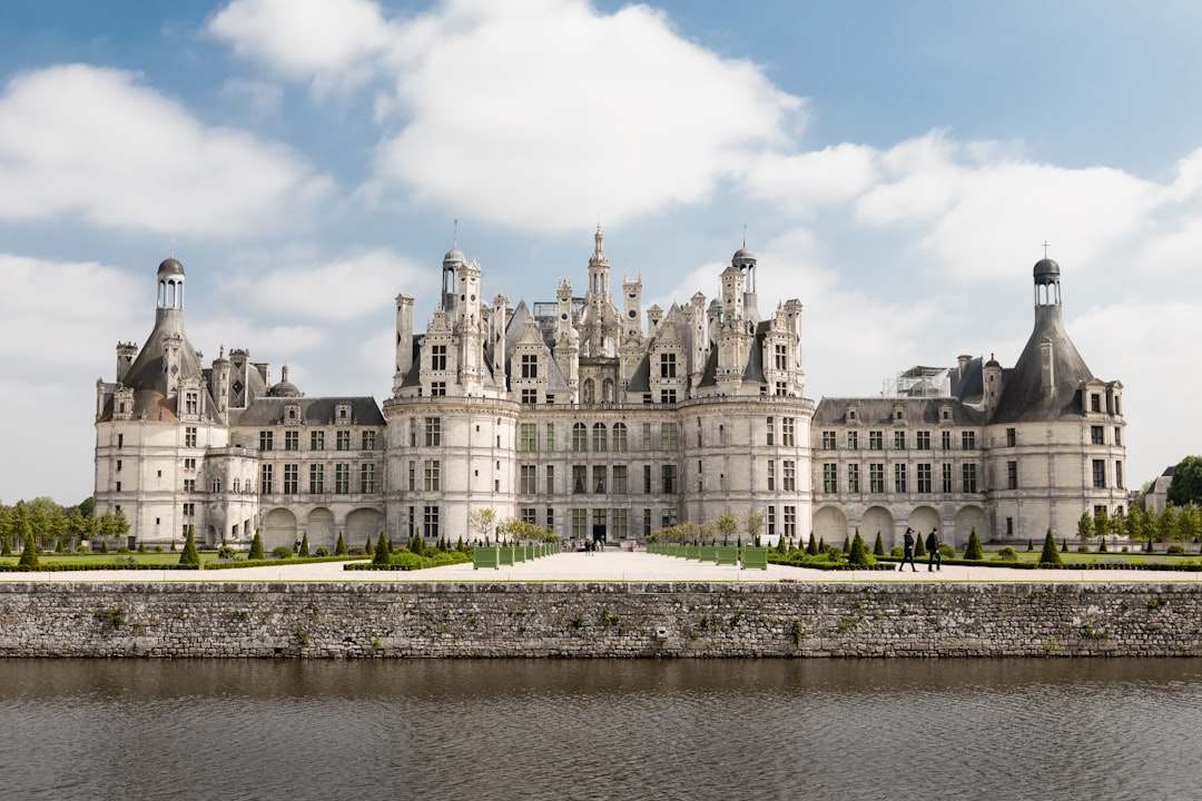 Chateau de Chambord in France, front view, with the river on one side and people walking along it, sunny day, blue sky with white clouds, high resolution photography, detailed, fine details, isolated plain background, stock photo, photography in the style of a professional with color grading, hyper realistic photography