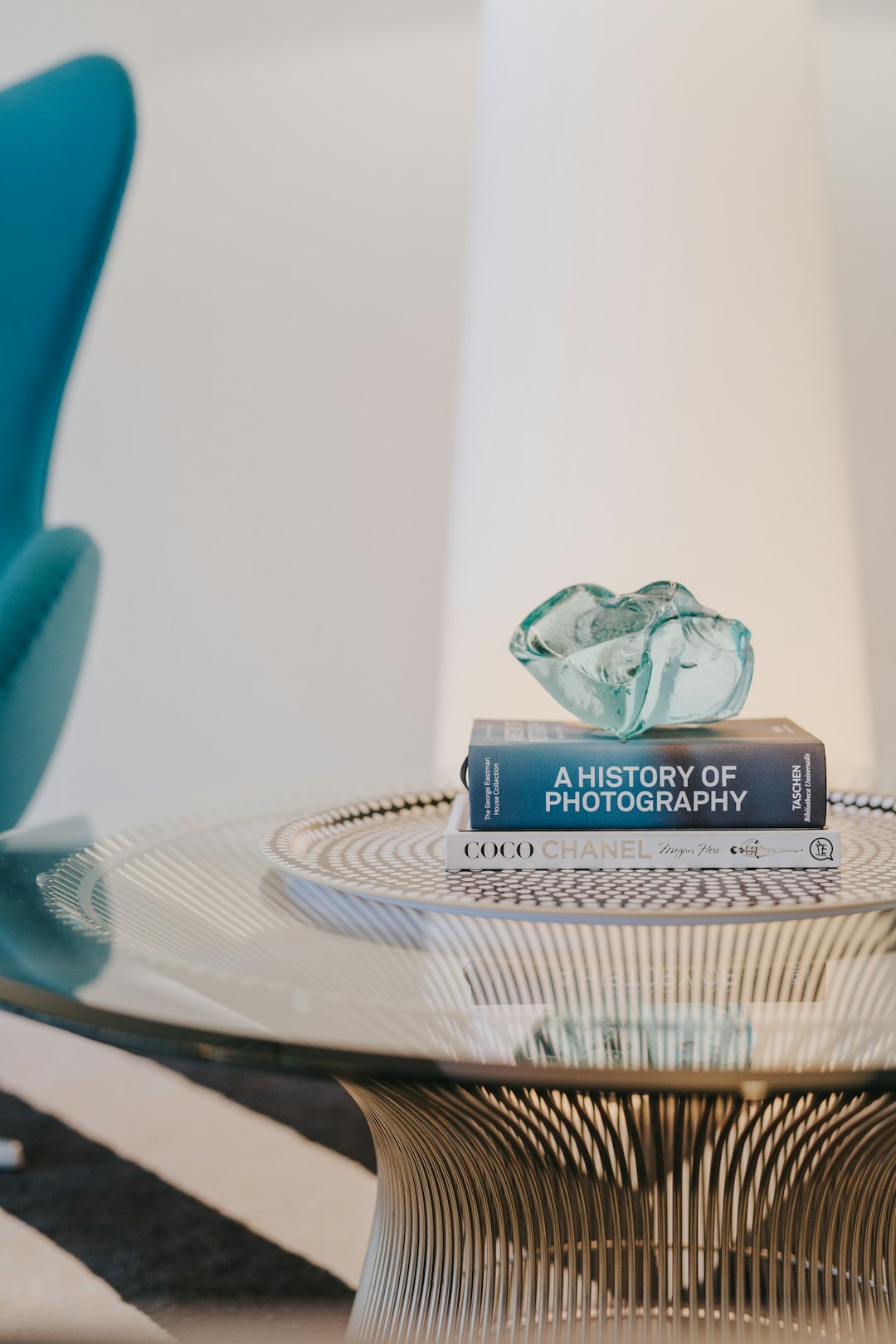 A close up photo of the book “A JD😃 resigns from desk photography” sitting on an elegant glass coffee table, with modern blue chairs in the background against white walls, in the style of a coffered ceiling design, with an abstract sculpture made of jade and gold sitting next to it, minimalistic, natural light, shot in the style of a canon eos r5. –ar 85:128