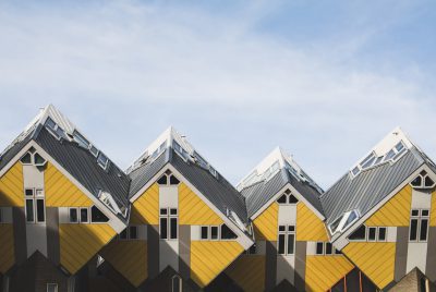 Photo of the several cube houses at right angles with gray roofs and yellow walls, all connected to each other forming one big house, in the style of raw style, square shaped houses, skyline view, clear sky, daylight, Amsterdam, unsplash photography.