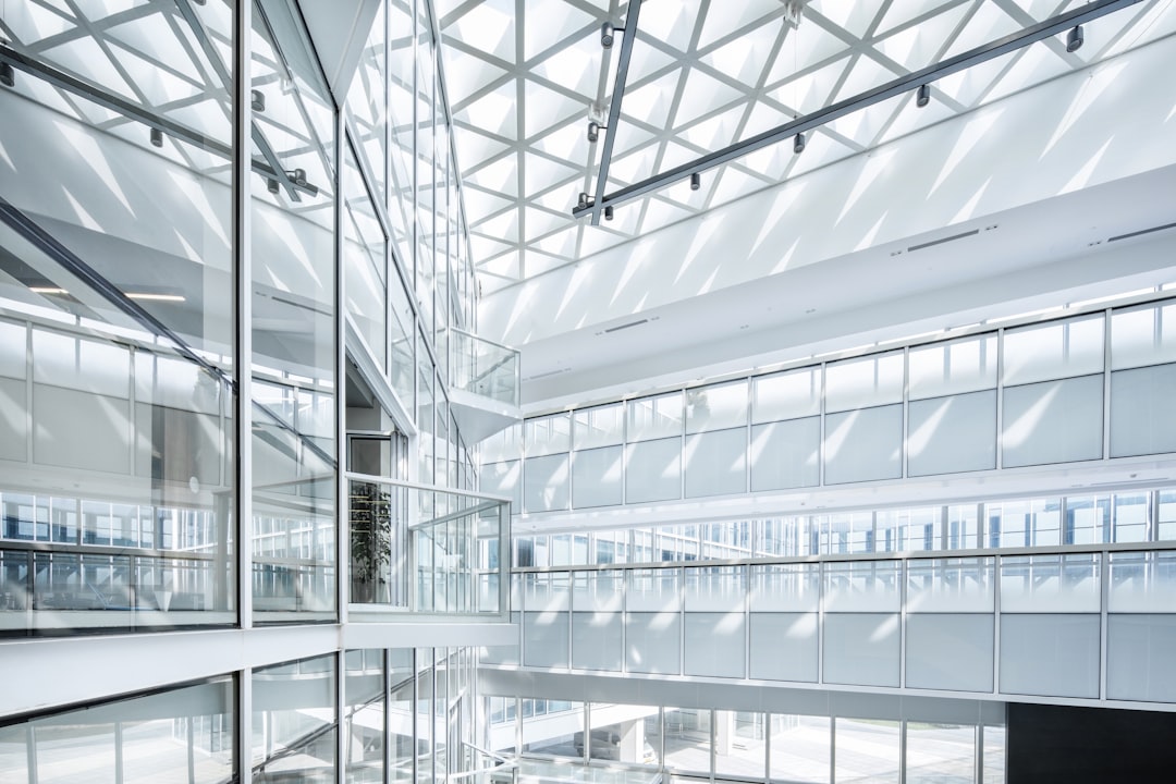 A photograph of an interior space in the style of [Tadao Ando](https://goo.gl/search?artist%20Tadao%20Ando) and [Anish Kapoor](https://goo.gl/search?artist%20Anish%20Kapoor). The interior has the form of a CEO’s global experience center located on the top floor of a high-tech building made from glass with skylights. The white steel structure features a meshing ceiling structure and a double height office lobby space with high ceilings. A white metallic structure grid ceiling lets sun rays come through, with suspended catwalks and glass curtain walls. The double height lobby leads to the main entrance door, photographed with a 35mm lens. –ar 128:85