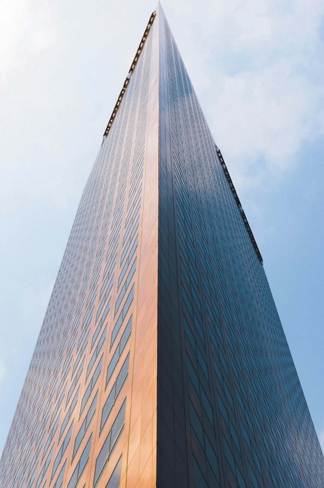 A tall building with an angular design, shot from the ground looking up at it. The exterior of it is made out of copper and glass. It’s a cinematic photograph shot on a Sony A7S III camera with natural lighting and bright colors in the style of no particular artist. –ar 85:128