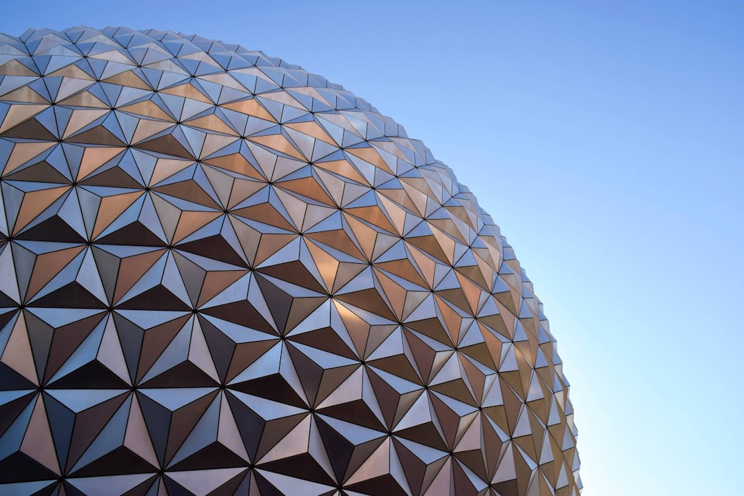 A closeup of the Epcot ball, showcasing its geometric pattern against a clear blue sky. The background is a clean and simple gradient from light to dark blue, creating contrast with the detailed textures on each side of the dome. This shot highlights the architectural design of Disney’s iconic building, offering an up close perspective that captures both elegance and complexity in the structure’s shape. –ar 128:85