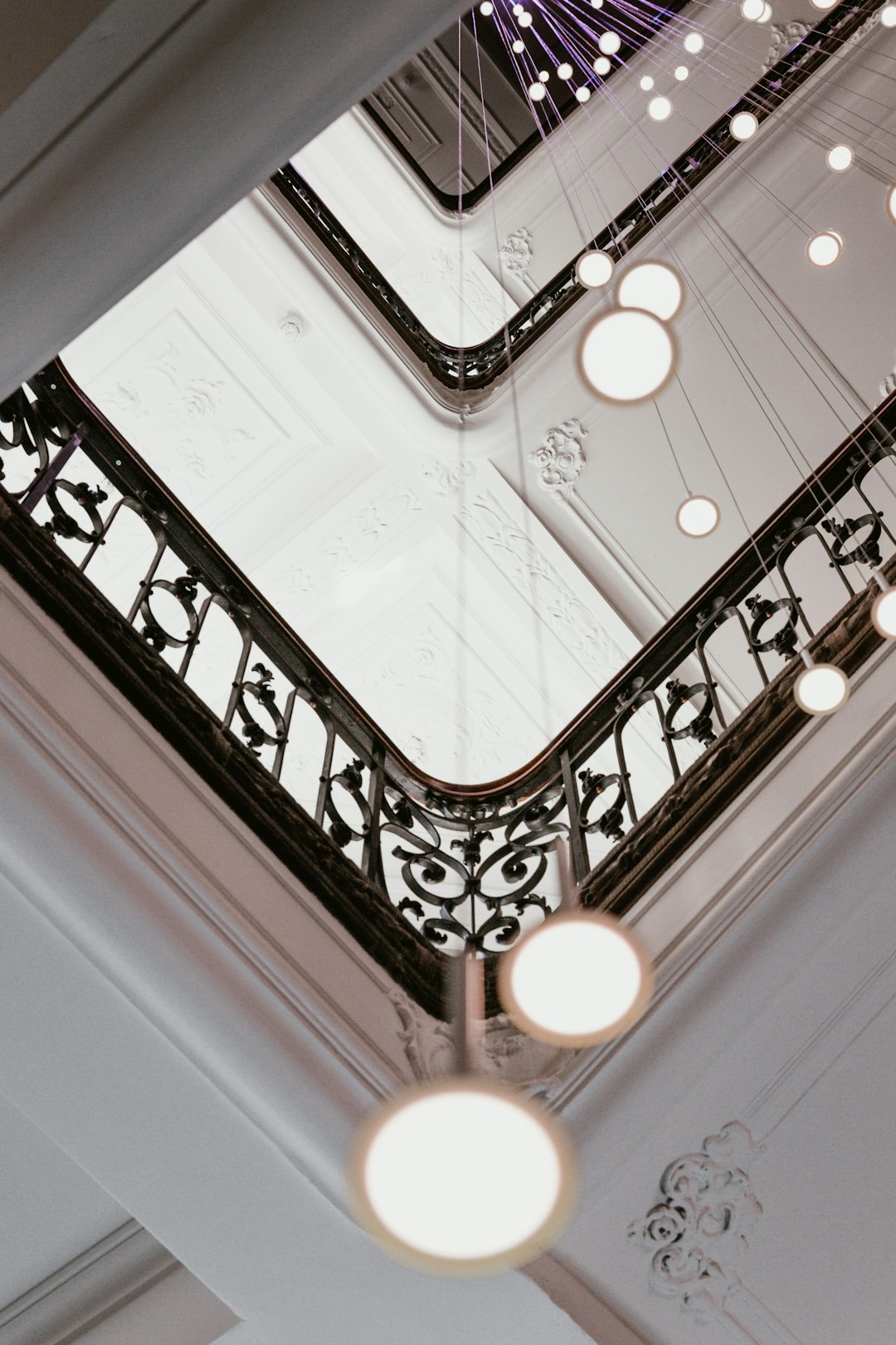 staircase, hanging lights, close up, ceiling view, luxurious hotel in paris, white walls, black iron details, purple accents, vintage style architecture, wide angle lens, cinematic –ar 85:128