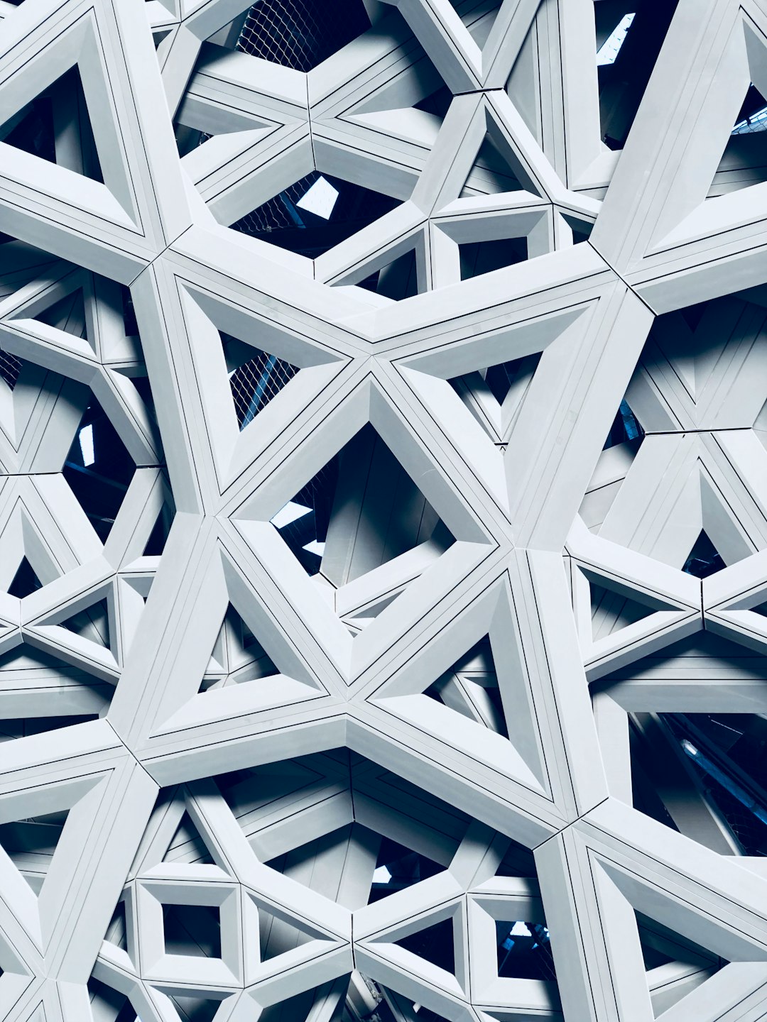 A closeup photograph of an architectural structure made from interlocking triangles and squares, creating intricate patterns in shades of white and silver. The building’s exterior is covered with these geometric shapes that form unique structures resembling stars or sacred geometry symbols. In the background, there’s a cityscape visible through the windows, adding depth to the scene. This composition emphasizes the symmetrical arrangement of shapes and highlights the elegance of modern architecture in the style of modern architecture.