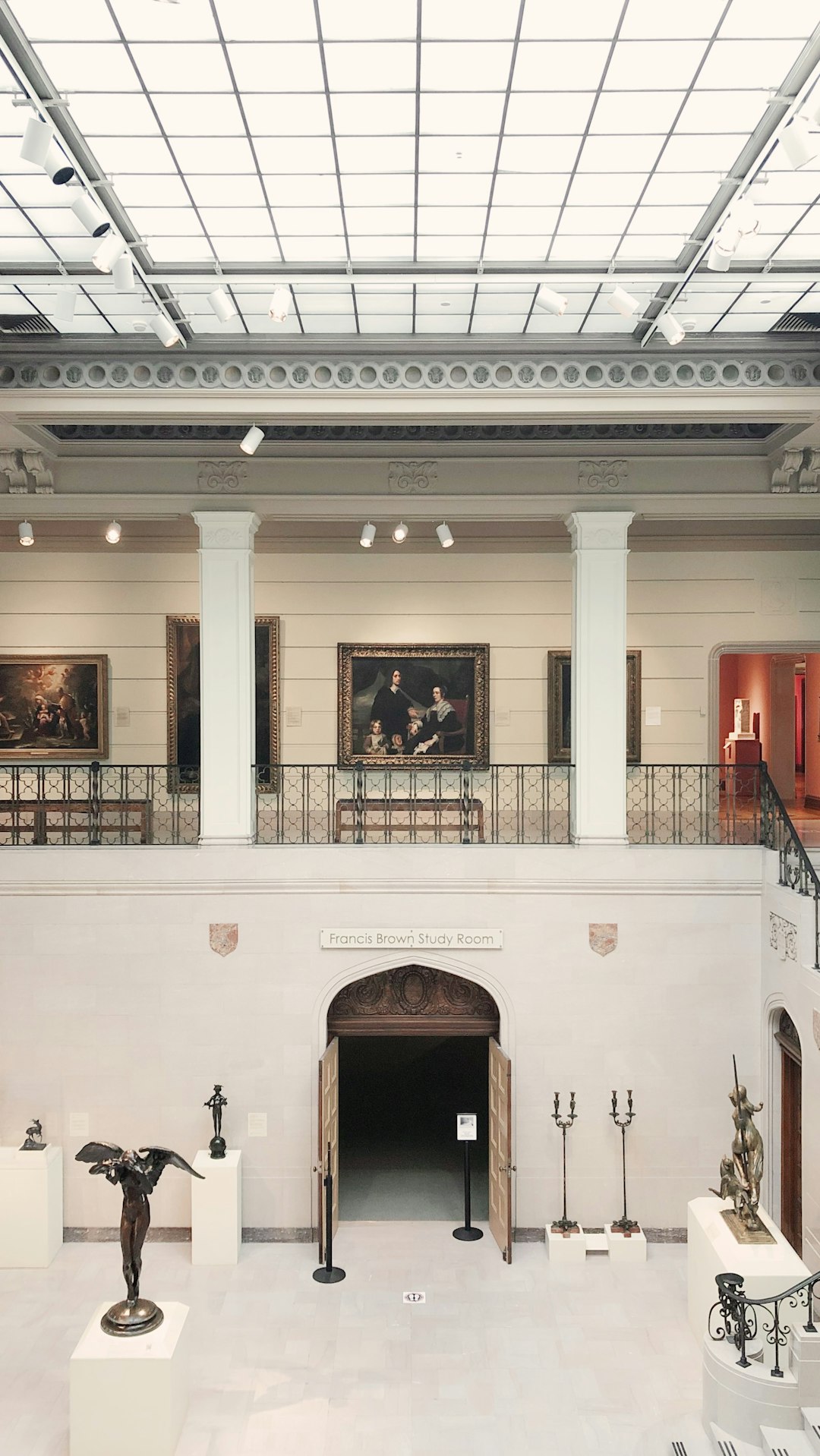 Photo of the top floor at Le Louvre with art and sculptures, white walls, glass ceiling, view from balcony to bottom level, paintings on wall, ” franz d Jose Fallon study room” sign above entrance door, large space, black metal railings, stone columns, modern lights, sculptures in corner, high ceilings, wide angle shot, architectural photography, –ar 9:16