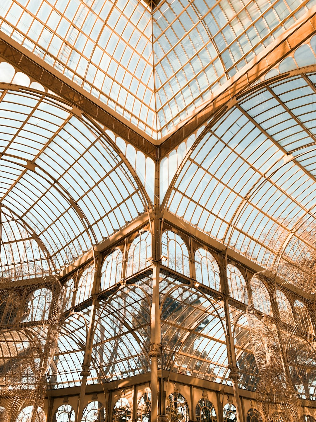 An architectural photo of the glass roof in the poetics and light of an old Victorian greenhouse with glass, steel beams, a ceiling that is all glass with beautiful light shining through. The interior has ornate ironwork and plants hanging from it. It’s in Madrid, Spain. Warm tones, sunny day, cinematic, editorial photography in the style of Madrid. –ar 3:4