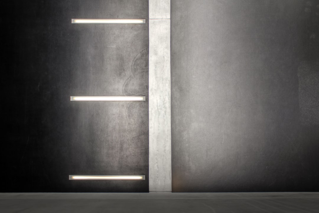 A minimalist wall with two white neon light strips on the right and left, set against an empty dark grey background. The lighting is soft yet powerful, casting gentle shadows that accentuate textures of concrete walls. A subtle hint of gray from the neon lights adds depth to the scene. This image portrays minimalism in interior design, focusing not just on the product but also its impact on space composition.