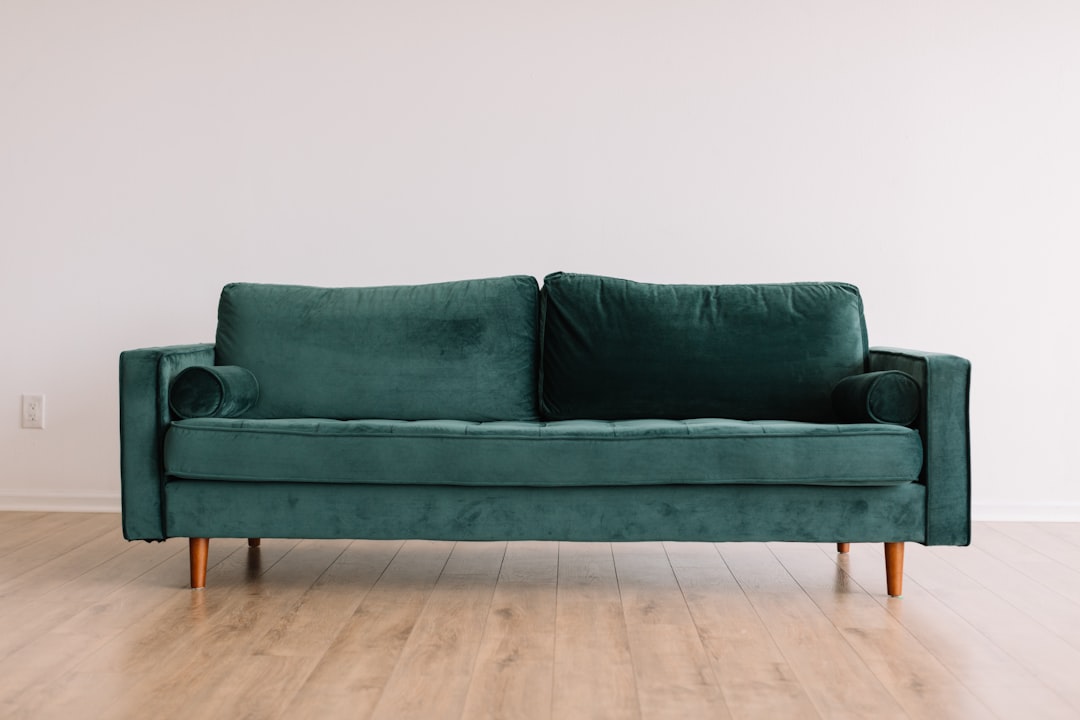 A simple dark green velvet sofa in an empty room with white walls and wooden floors, shot from the front at eye level, showcasing its elegant design against a clean background. The sofa is centered in the frame, highlighting its soft texture and luxurious color in the style of no artist.