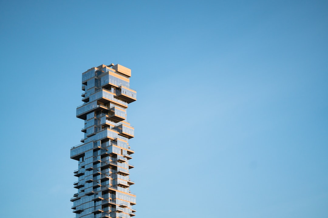 A tall building made of geometric shapes stands against the blue sky, shot from afar. The photo was taken with Canon EOS R5 and has a minimalist style in the style of geometric shapes. –ar 128:85