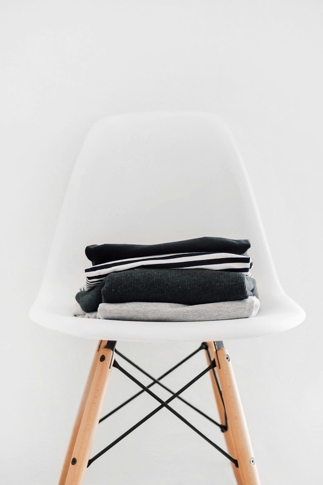 A stack of black and grey on top of a white chair, with a white background, in a simple minimalist photographic style, depicting a white modern Eames dining room setting, focusing on the . –ar 85:128