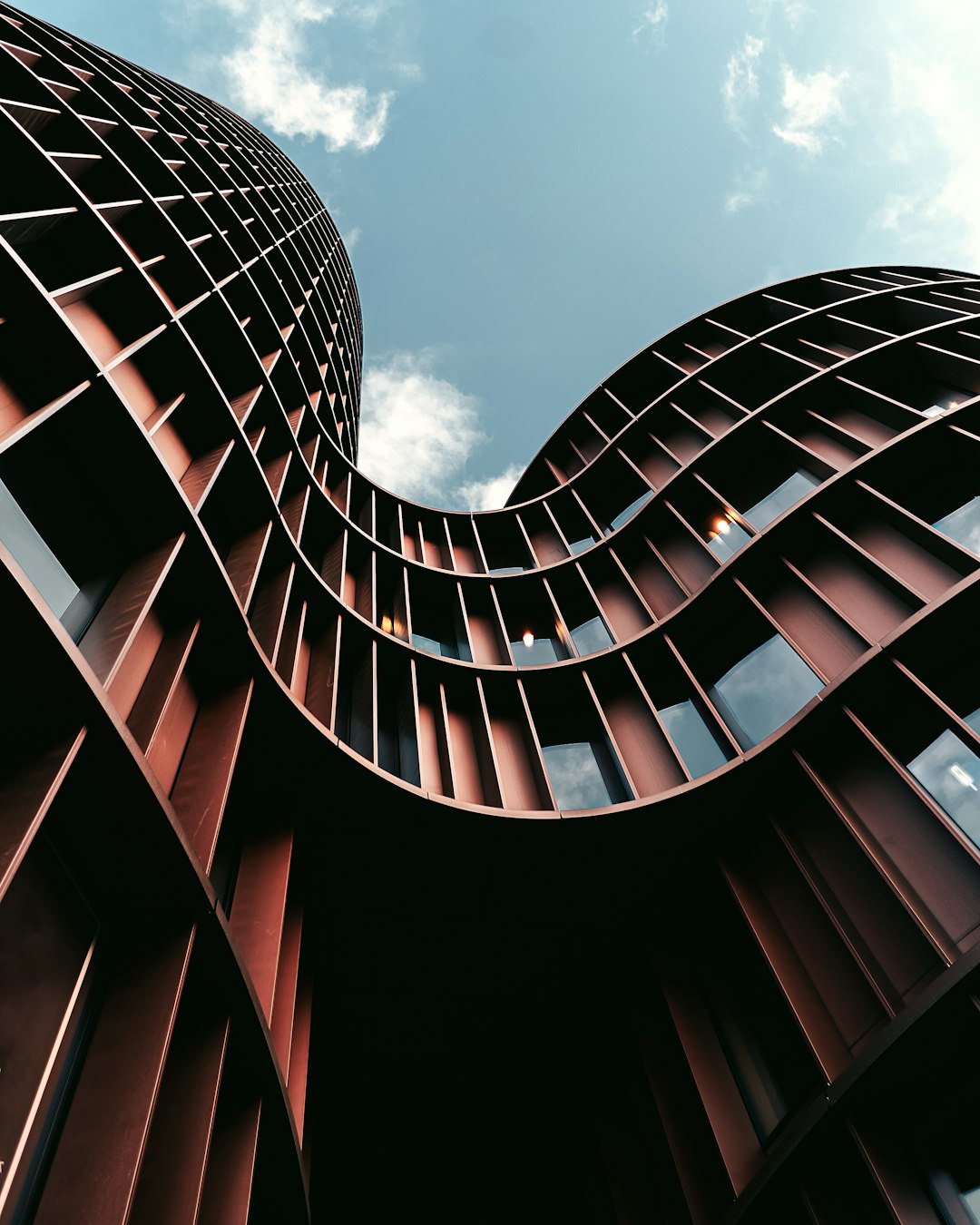 Modern architecture, exterior view of a curved building with brown metal panels, low angle shot, blue sky background, cinematic shot in the style of michael bay