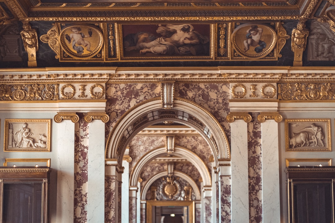 A photo of an archway in the grand hall, with paintings on the wall and marble columns, gold trim around it, in the baroque style and with a barternal aesthetic, shot in the style of canon eos r5. –ar 128:85