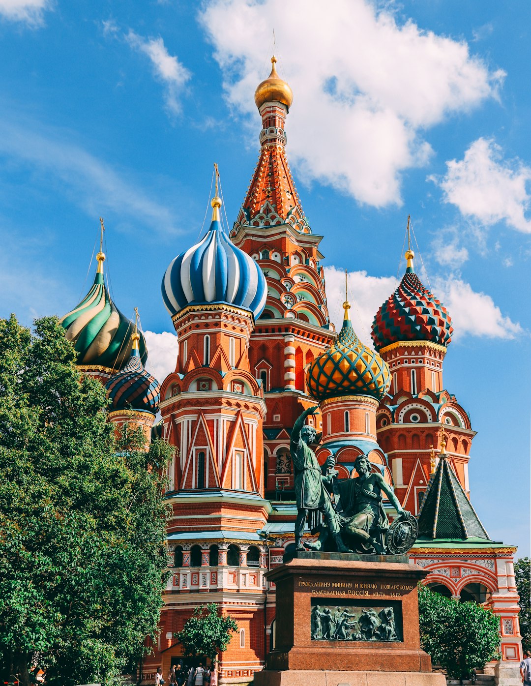 Sint Ork lounge style photo of St Basil’s Cathedral in Moscow, on a summer day with a blue sky, the domes have colorful ocular designs, there is an impressive statue and monument on one side of it, green trees surround the cathedral, in the style of unsplash photography. –ar 99:128