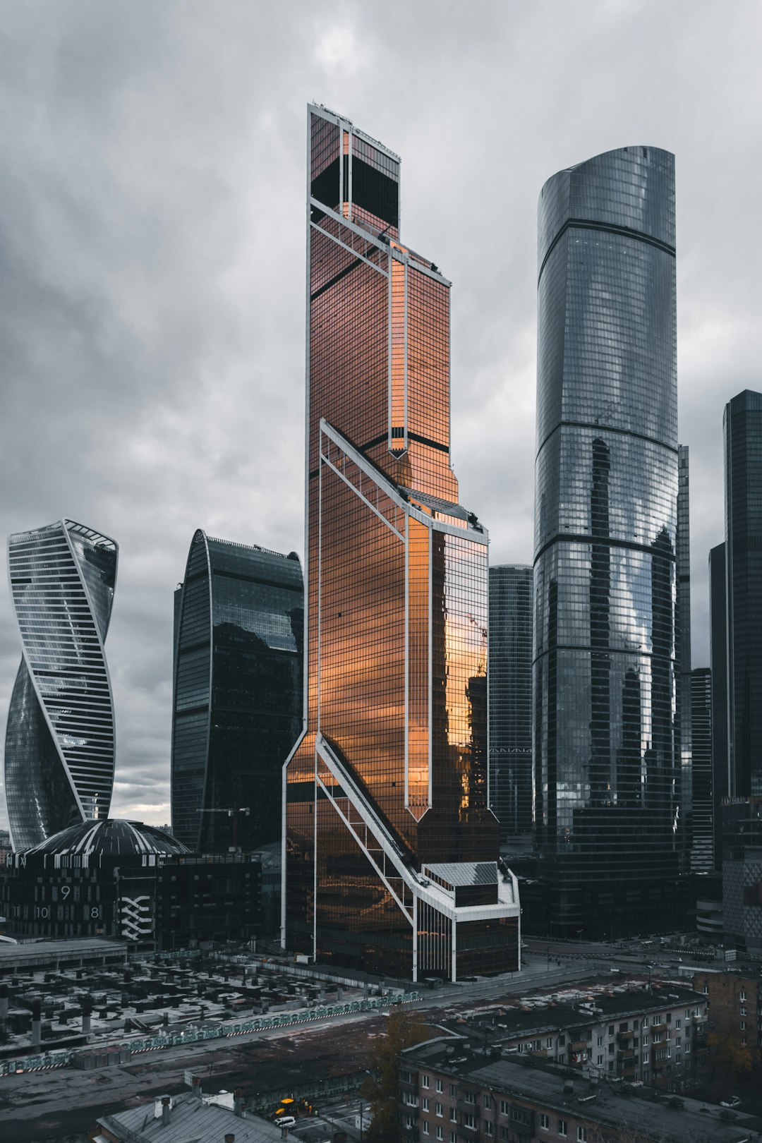 A skyscraper in the Moscow City industrial district, made of copper and glass with an angular design. The building stands tall against grey clouds, surrounded by other modern buildings. In front is an empty square, leading to the entrance of another highrise structure. This photo was taken from above using a Canon EOS R5 camera, capturing every detail of its architecture in the style of modern architecture. –ar 85:128