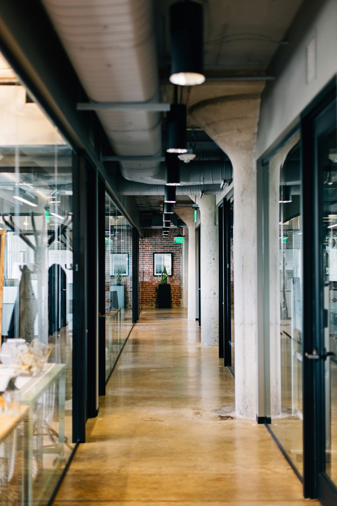 A photo of the interior design of an office space in Los Angeles, showcasing industrial style architecture with glass walls and concrete floors. The focus is on a long hallway leading to various rooms where employees work at their desks. There’s an emphasis on natural light coming through large windows, creating soft shadows and highlights that highlight details like vintage decor and unique art pieces. This shot captures the essence of contemporary urban life within the building. –ar 85:128