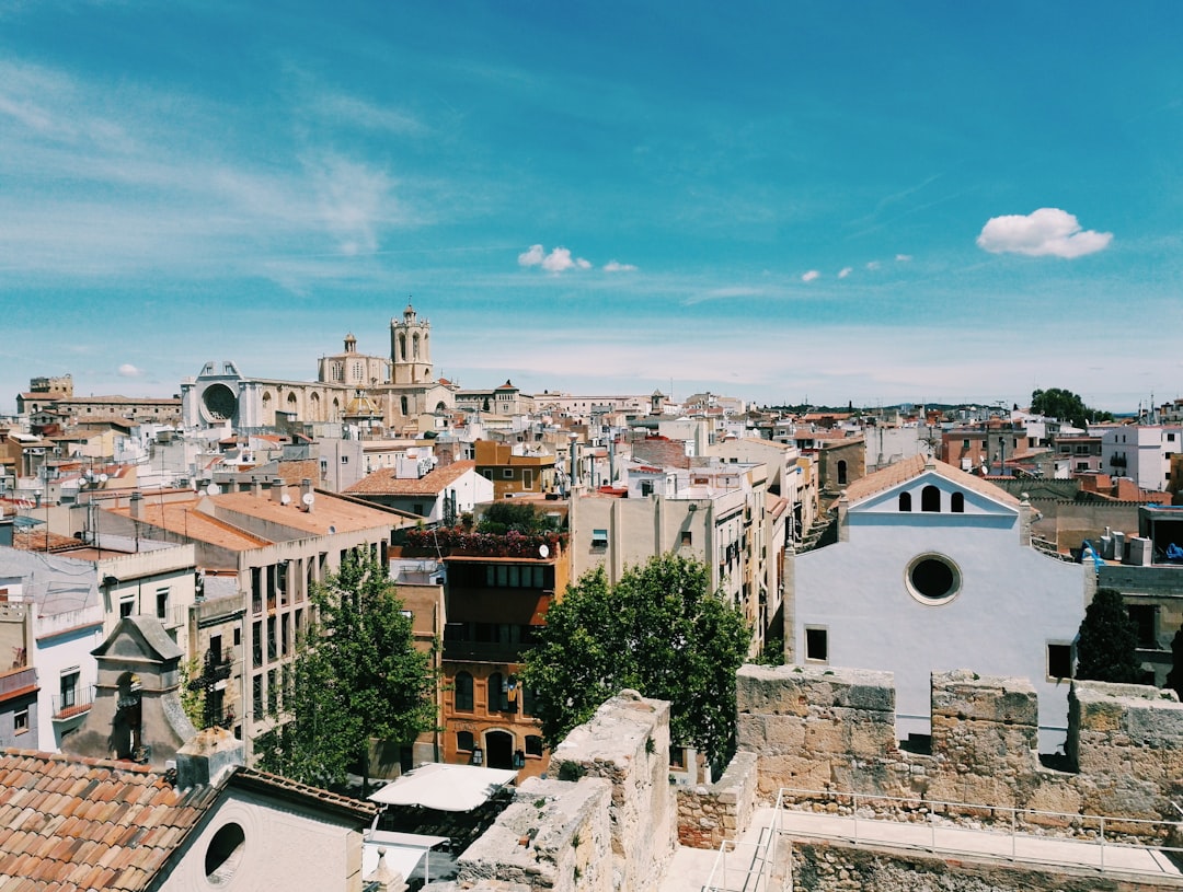 The view of the city from above, in the photograph style. In the style of Monrsco de la Puea del C gorgeous buildings and streets with a church in one corner. The sky is blue with some clouds. There’s an old white building on the right side. A beautiful sunny day. The photo was taken in the style of a professional photographer using a Fujifilm XT4 camera with a 23mm f/8 lens at a Fisheye angle. It has very high resolution and detail.