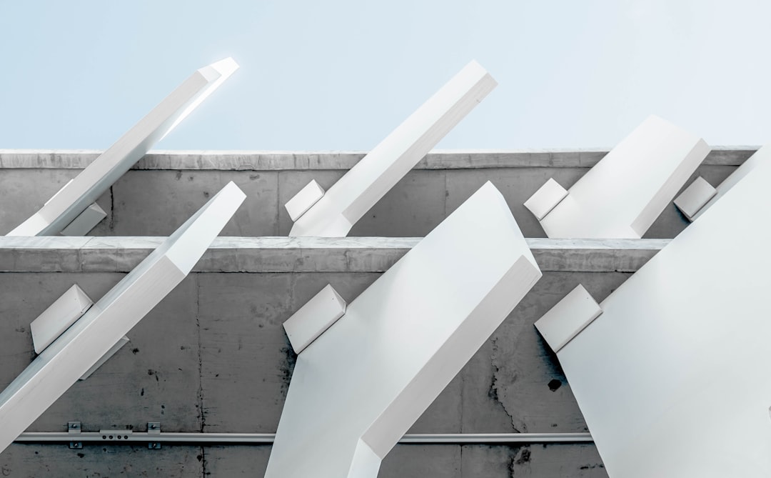 A minimalist photo of white architectural elements on the roof, with sharp angles and geometric shapes, against an empty background. The focus is placed in front of two angular structures that appear to be connected in the style of several large concrete beams, creating an abstract composition that emphasizes form over color. –ar 128:79