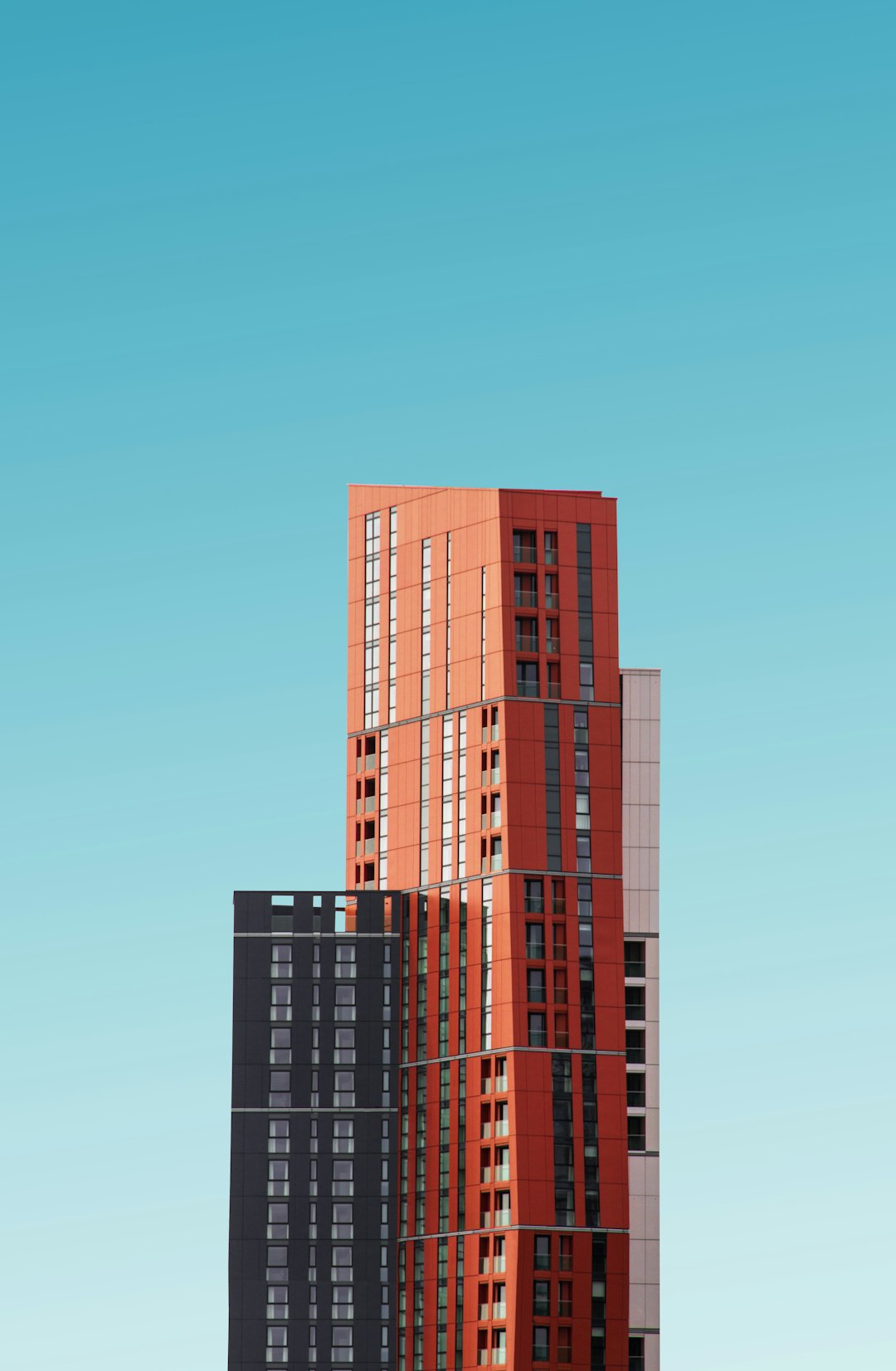 A tall building with red and black colors against the blue sky, minimalist photography in the style of orange tone, simple background, high resolution –ar 83:128