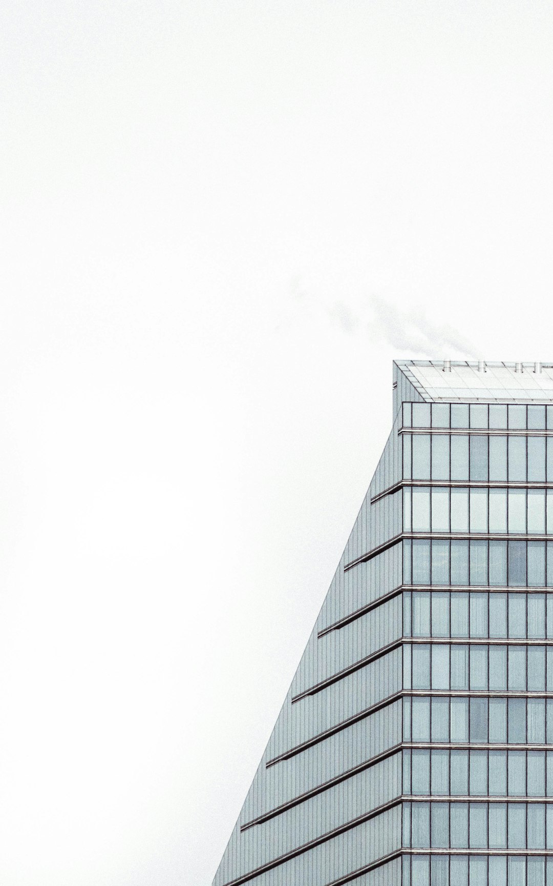 A modern building with a minimalist design is shown in a closeup shot against a white background. White smoke is rising from the top of one corner. Clear details and high resolution photography give it an architectural magazine style. A high angle view shows the minimalist and geometric composition. High contrast lighting and professional color grading use cool tones, focusing on the glass windows and metal surfaces. The style is reminiscent of minimalist architectural photography. –ar 5:8