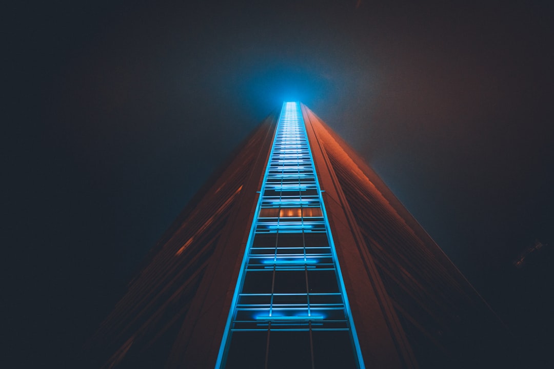 low angle photo of tall blue ladder leading up to the sky, skyscraper at night, orange light from top left, cinematic, unsplash photography style, dark moody lighting