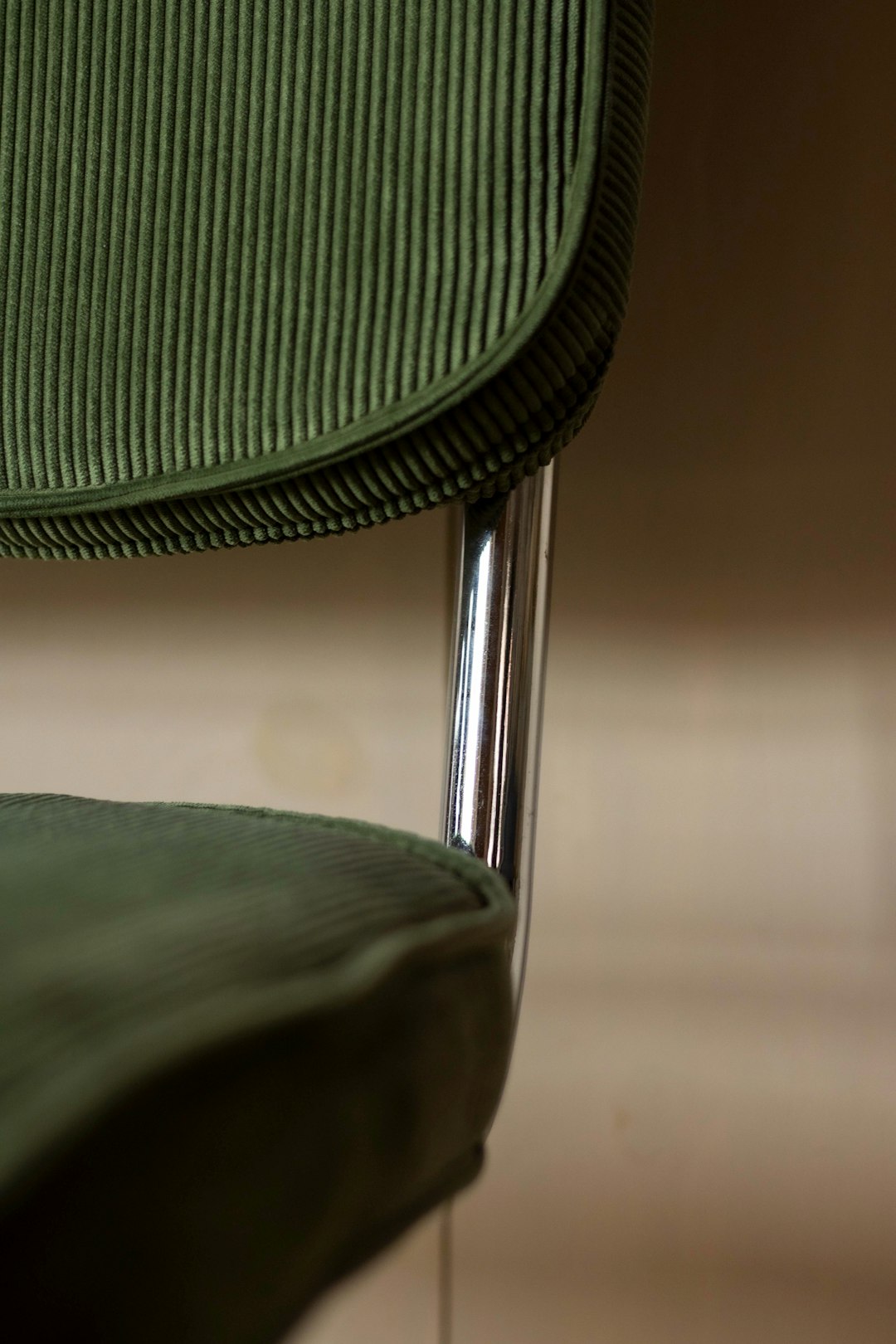 Close up detail of a green corduroy dining chair with chrome legs, in the style of minimalism, editorial photography, shadowplay, on a beige background. –ar 85:128