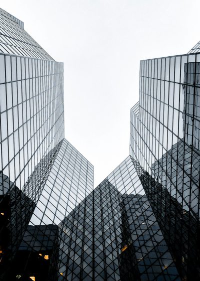 Photo of two skyscrapers at a diagonal angle against a white background, showing the glass and steel architecture of a modern cityscape in a minimalist style of photography. The architectural design features glass panels on the buildings creating geometric patterns and symmetrical reflections. The high resolution image was captured in the style of Sony Alpha A7 III camera with a Zeiss Batis lens at an aperture of F/2, under soft lighting.