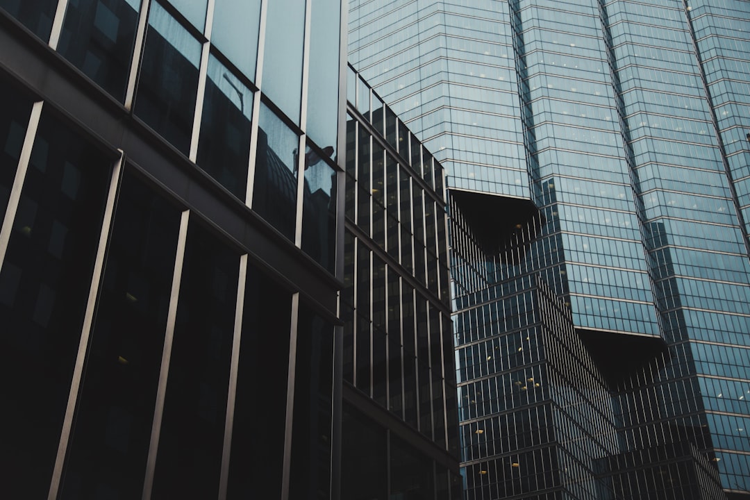 A closeup of the exterior walls and glass windows of an office building in downtown Tokyo, Japan. The architecture is modern with sleek lines and large window panes that reflect other buildings nearby. In the background there’s another tall skyscraper with black metal frames. It captures details like reflections on polished surfaces, light play between dark shades, and architectural elements such as steel beams and cables visible through transparent panels. Shot in the style of photographer Alex Strohlachmmer using a Sony A7R IV camera. –ar 128:85