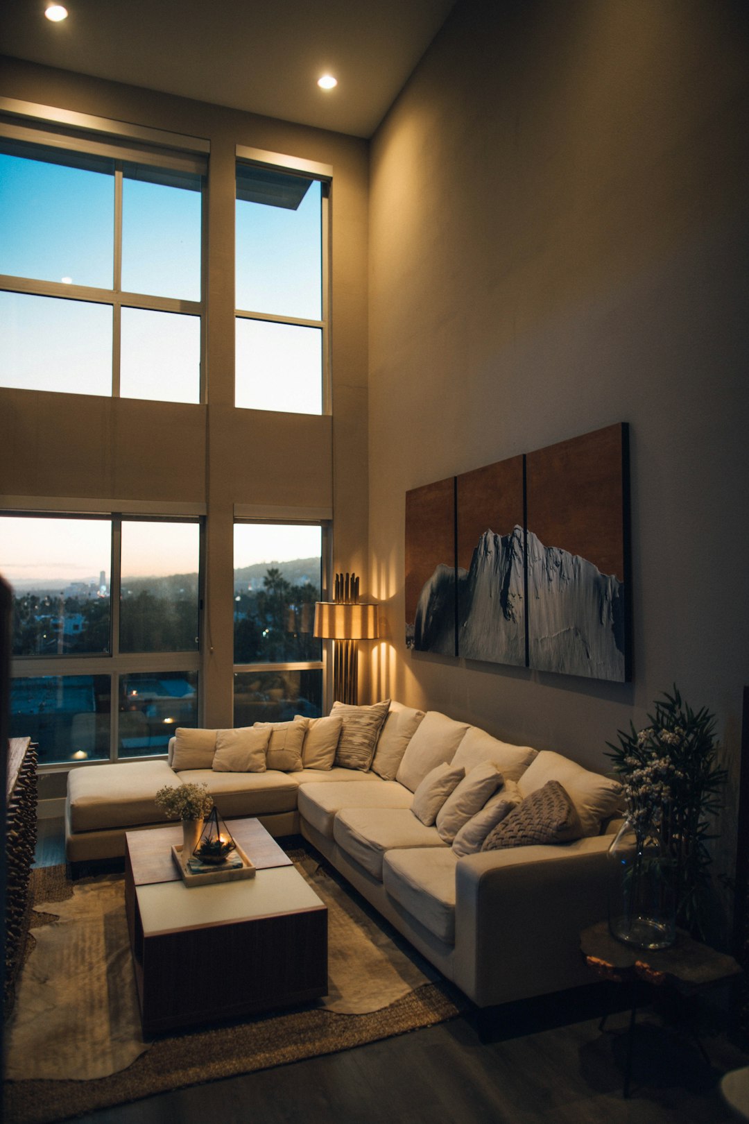 modern living room with large windows, a sofa and coffee table, wall art hanging on the walls, warm lighting, night time, high angle shot, architectural photography. The wall art is in the style of various artists. –ar 85:128