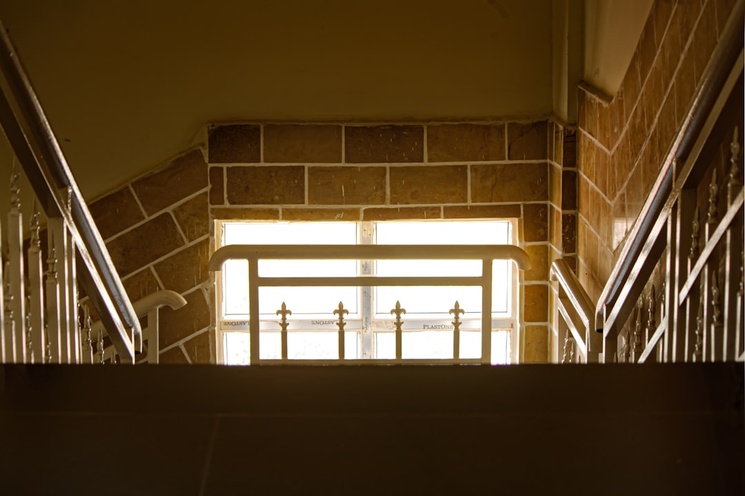 View from the top of an iron staircase leading to a window with light coming through, brown brick wall, cream colored tile, low angle, close up, warm lighting, symmetrical. –ar 128:85