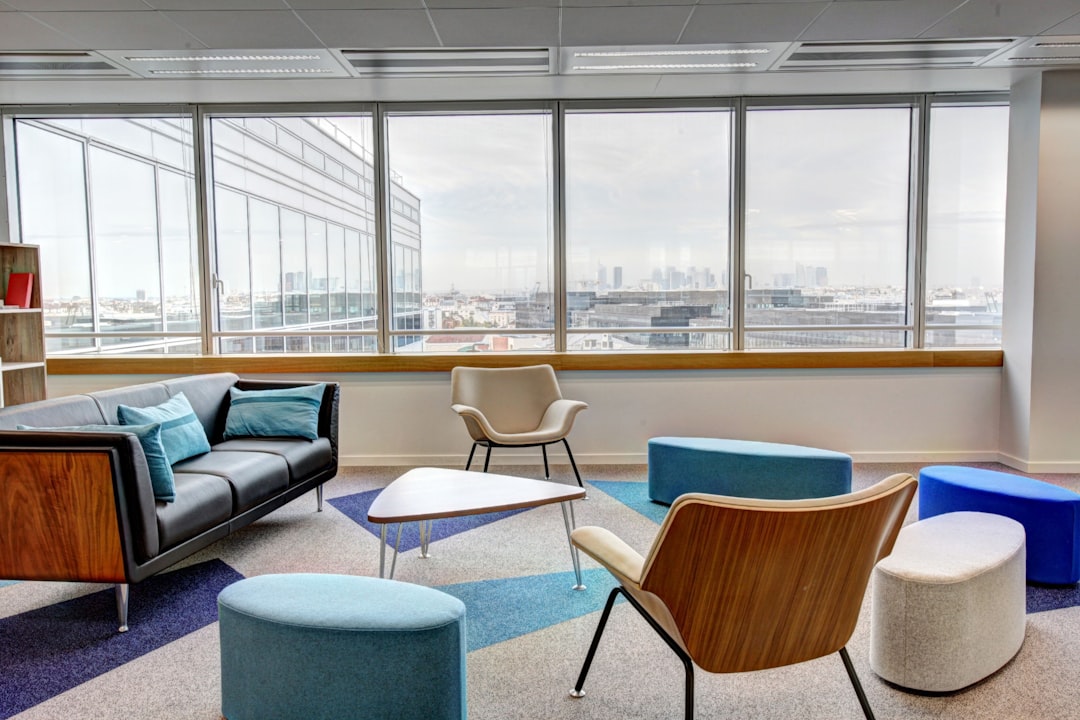 A photograph of an office lounge area with modern furniture, large windows overlooking the city skyline, and comfortable seating areas for employees to socialize during coffee break time. The room is well lit by natural light from outside, creating a bright atmosphere. In blue tones with accents in turquoise and purple. Taken on a Canon EOS R5 camera with a 24-70mm f/8 lens at an aperture of f/6, in the style of minimal editing of the original text. –ar 128:85