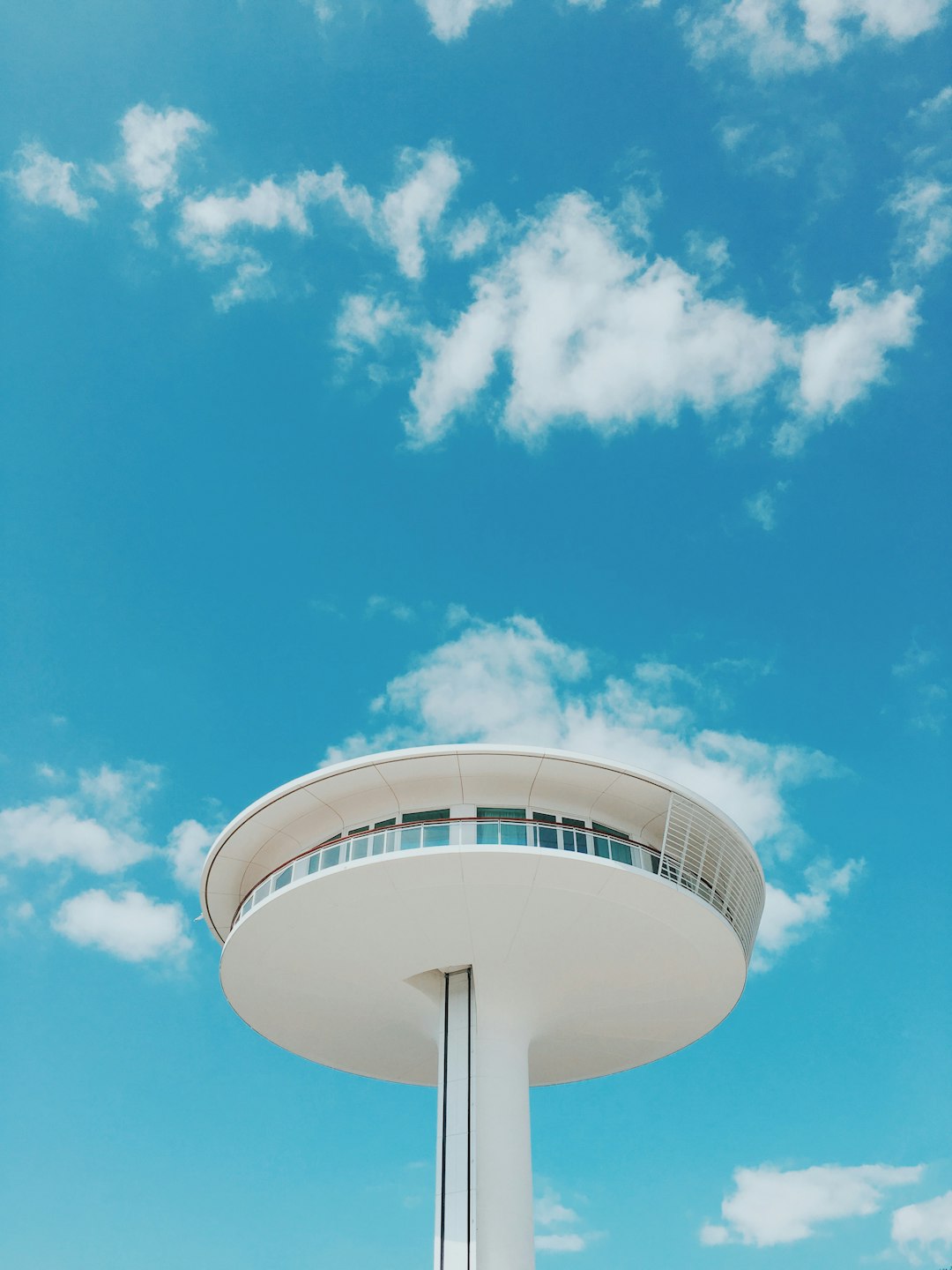 White circular water tower in Tokyo, blue sky with clouds background, minimalist photography, white and beige, low angle shot –ar 3:4